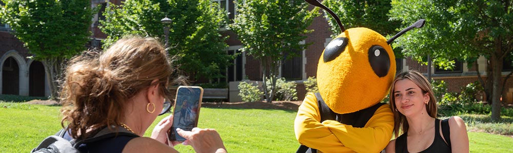 A student poses with Buzz, Georgia Tech’s yellow jacket mascot, while someone else takes a photo of them on a smartphone.