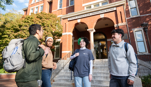 A group of four undergraduate students stand and chat at the bottom of Tech Tower on Georgia Tech’s campus.