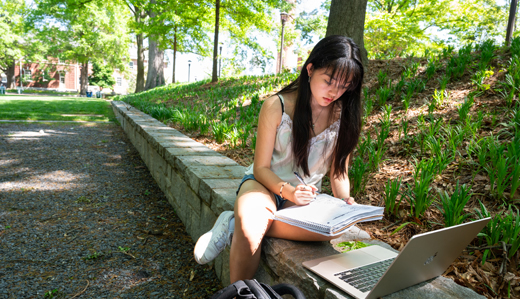 A Georgia Tech undergraduate student works on her laptop in a green space located just below Tech Tower on campus.