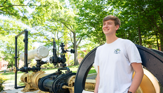 A Georgia Tech student leans against an old steam engine on campus painted gold, black, and white