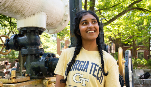  An undergraduate student wearing a yellow Georgia Tech t-shirt poses near an old steam engine on campus.